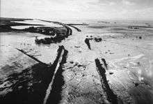 A river flows past between broken levees, spreading over an extensive flat landscape before continuing to the ocean