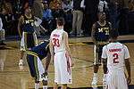 Two opposing basketball teams on a basketball court with a team in dark blue uniforms at the free throw line. One team is in white uniforms with names on the back and the other is dark blue with the word Michigan on the front and names on the back.