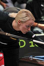 Woman leans over a table with a pool cue in her hand