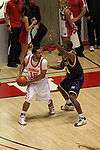 A basketball player in a dark blue uniform is defending against a player in a white uniform.