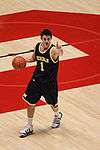 A basketball player in a dark blue uniform is dribbling the basketball and signalling with his index finger.