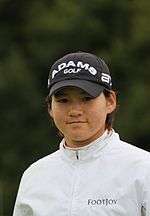 A brown-haired woman in a white jacket and a black cap