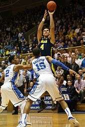 Player shooting, guarded by two opponents