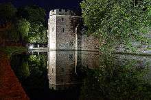 Night scene of floodlight stone walls adjoining still water.