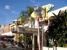 A photograph of a white building with a pink, green, and yellow television-shaped sign in front of it reading "50's PRIME TIME Cafe" in stylized letters