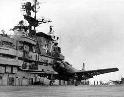 A propeller-driven aircraft prepared to take off aboard an aircraft carrier deck.