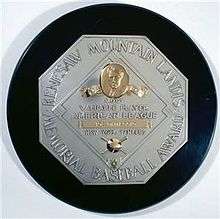 A black circle with an octagonal silver plaque in the middle. The edge of the plaque reads "KENESAW MOUNTAIN LANDIS MEMORIAL BASEBALL AWARD". In the middle of the octagon is a baseball diamond which contains, from the top, Judge Landis' face in gold, "Most Valuable Player", the winner's league, his name in a gold rectangle, and his team.