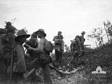 Soldiers wearing slouch hats and carrying rifles form up below a ridge line