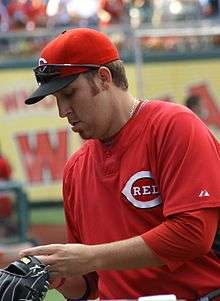 A man in a red baseball pullover and red baseball cap with a white "C" on the front signs a baseball with his right hand.