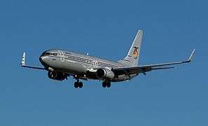 Left side view of the front of an aircraft painted dark gray with blue sky in the background.