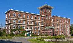 A brick building with two offset wings and a higher tower in the center with a peaked green top