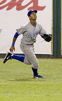 A man in a blue baseball uniform with a navy hat enters the baseball field