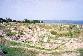 Remains of walls of small structures are seen in the foreground, while the Southern Bug estuary is seen in the background.