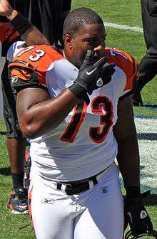 An American football player wearing a white and orange jersey with the number 73 across the chest with his hand in front of his face.