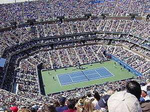 A tennis stadium pack with fans watching a grass court.