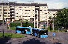 Blue articulated bus, with long five-story building in background