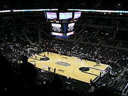 The inside of an arena with large scoreboard visible, which is set up for basketball.