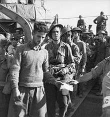 A line of unarmed soldiers disembarking from a ship down a gangway.