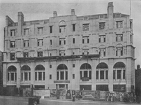 A long stone-faced façade with seven bays of windows, arched at first floor level and decreasing in size on the floors above. Prominent chimneys project above from the façade.