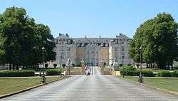 A giant stretch of road leads to an open gate enclosing a large palace.