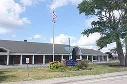 A blue sign with bold, gold serif lettering reading "BARRINGTON HIGH SCHOOL" stands in front of the school.