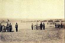 Photograph showing a line of artillery batteries standing at the ready in the foreground with cavalry and other troops massed in the background