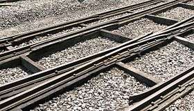 Three rails cross the picture from left to right supported on thick timbers; occasional smaller timbers cross between these and stone chippings fill the space between them.