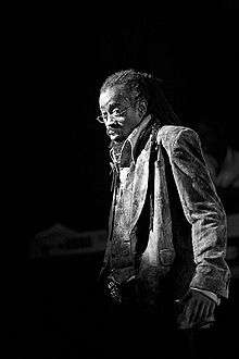 Black and white image of a man with dreadlocks wearing eyeglasses.