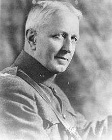 A black and white image of Ben Fuller, a white male in his Marine Corps dress uniform. He has white hair and is not wearing a hat. The background is cloudy and the outside edges of the picture are grayed out.