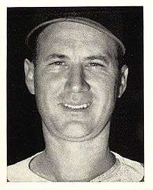 A close-up of a smiling man wearing a baseball jersey and cap.