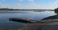 Lake with concrete boat ramp, small dock, more docks with boats in distance