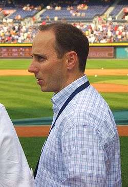 A profile of a man with brown hair and a white and blue button down shirt