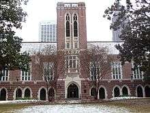 A wide, red brick building with a tower in the center and grey concrete archways spaced along the length of the building.