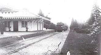 A train on a single rail track near a small white wooden station.