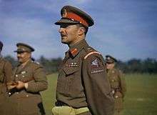 Half length portrait of a man wearing a military uniform a peaked cap with scarlet band. He wears the airborne forces patch on his sleeve.