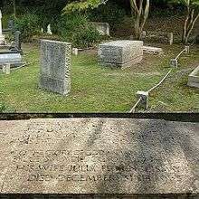 A fenced patch of grass in a cemetery with four headstones of different shapes