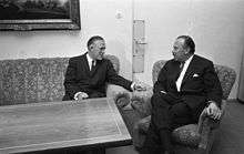 Two middle-aged men sitting in a sofa and a chair around the corner of an empty table