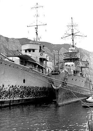 two naval ships moored alongside each other with mountains in the background