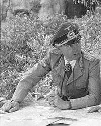 A man wearing a military uniform, peaked cap, and an Iron Cross displayed at the front of his uniform collar.