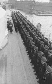 Two men walking by a row of men on the side of ship.