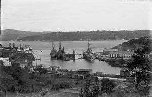 A large warship is tied to the dock in a narrow channel of water.