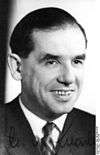 Black-and-white portrait of a smiling man in semi profile wearing a suit and tie.