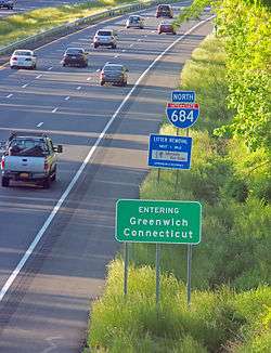 Three signs along a busy freeway. The one at the bottom says "Entering Greenwich Connecticut". The one above it has "Litter Removal" on it. The last one, at the top, is irregularly shaped with the number 684