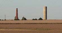 Tall brick chimney and cylindrical concrete water-tower standing alone in cornfield