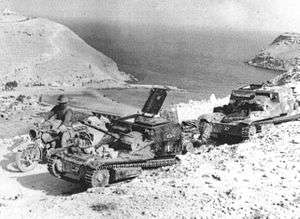 Soldier in steel helmet on a motorcycle rides past two small tracked vehicles.