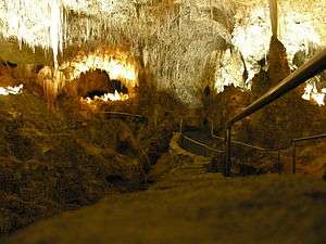 A picture of a partially illuminated underground cave with a jagged rock ceiling and a walkway extended into the cavern.