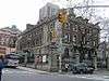 A three story brick and stone building sits on a corner in New York City and is surrounded by a stone and wrought iron fence.