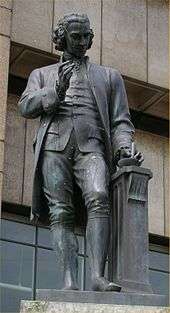 Statue of a man with a mortar and pestle in his left hand and his right hand upraised