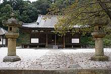 Wooden building with slightly raised floor, white walls and a hip-and-gable roof.