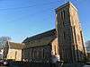 A long, flint-built church with a tall squared-off tower in the foreground, seen from close proximity.